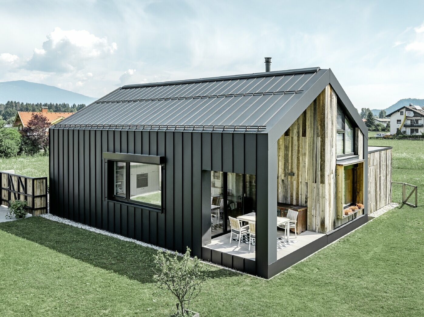 Detached house with gable roof, roof and façade are covered with PREFALZ from PREFA in P.10 anthracite. The panels of the roof surface extend across the façade. Part of the façade is clad with weathered wood.