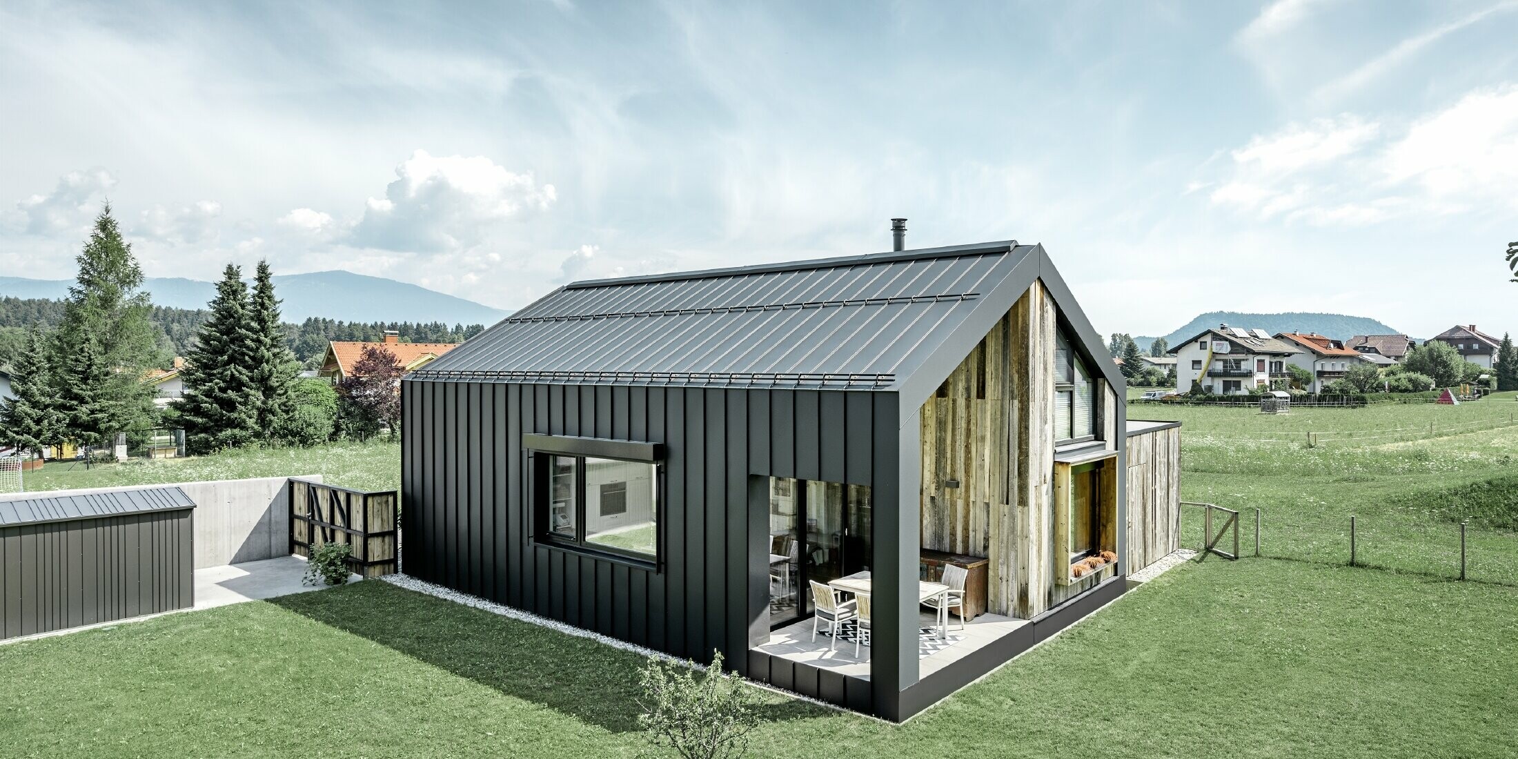 Detached house with gable roof, roof and façade are covered with PREFALZ from PREFA in P.10 anthracite. The panels of the roof surface extend across the façade. Part of the façade is clad with weathered wood.