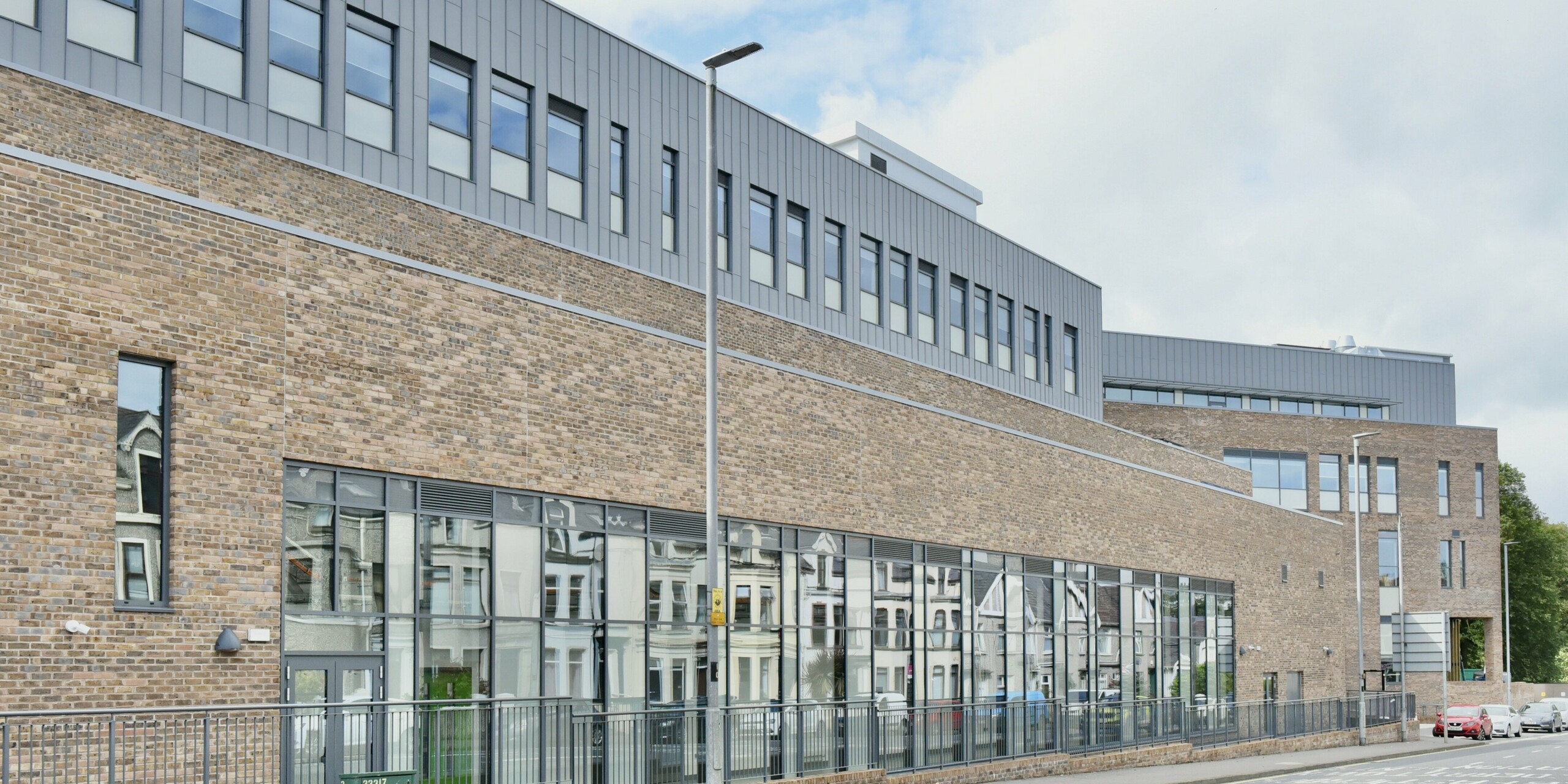 Street view of the North Regional College in Coleraine, Northern Ireland. The precisely crafted PREFALZ aluminium facade in patina grey complements the traditional architecture and harmonises with the classic brick look. Functionality and design combine to create an impressive building.