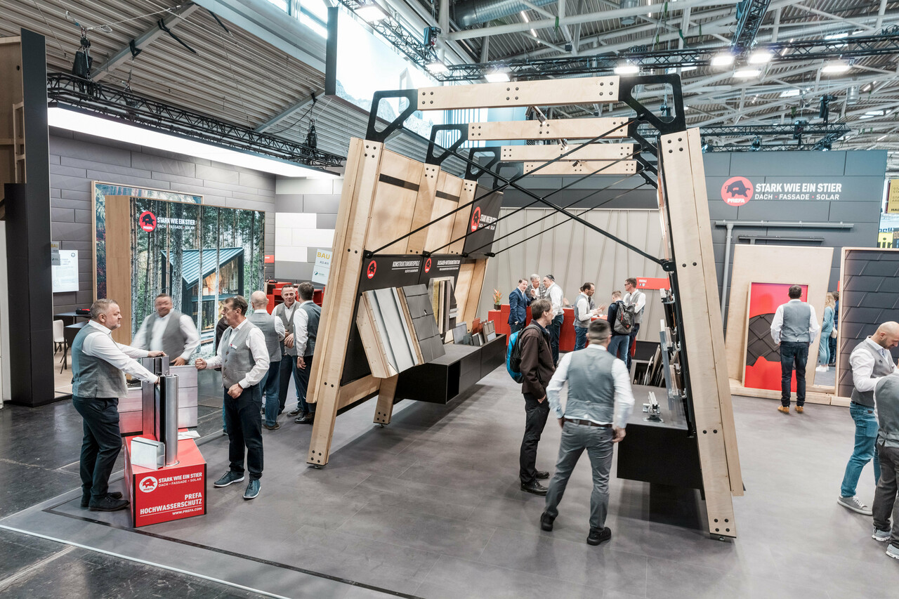 A bustling PREFA exhibition stand featuring display panels showcasing PREFA’s aluminium roofing and façade products.