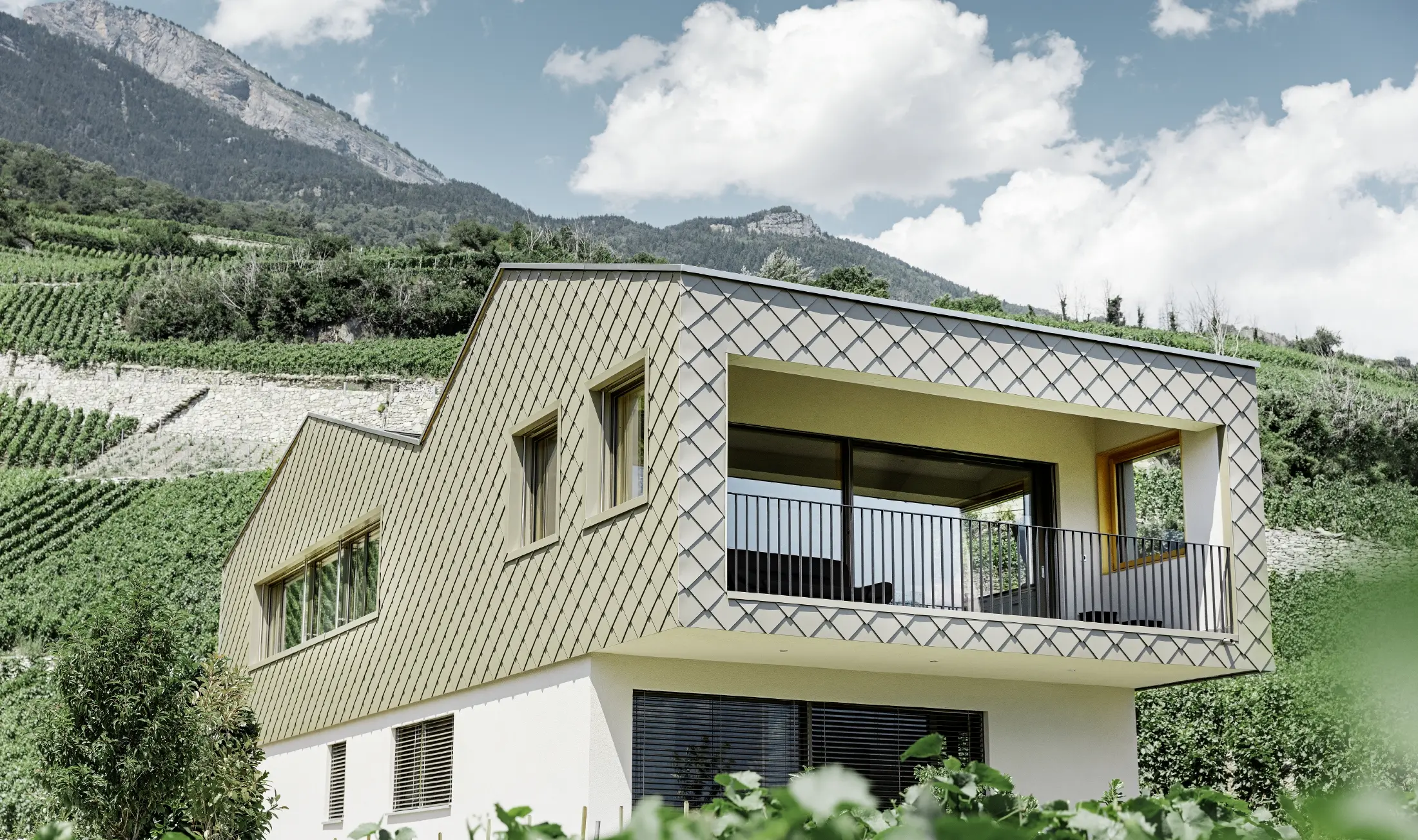Modern detached house set in the heart of the Rhone valley vineyards with four different roof surfaces and an open gallery clad with rhomboid façade tiles in bronze