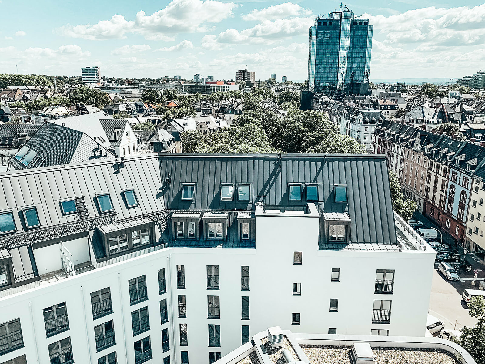 Far view of the finished renovated house in Germany. The roof in this side is clad with Prefalz in the colour P.10 zinc grey. A skyscraper can be seen in the background.