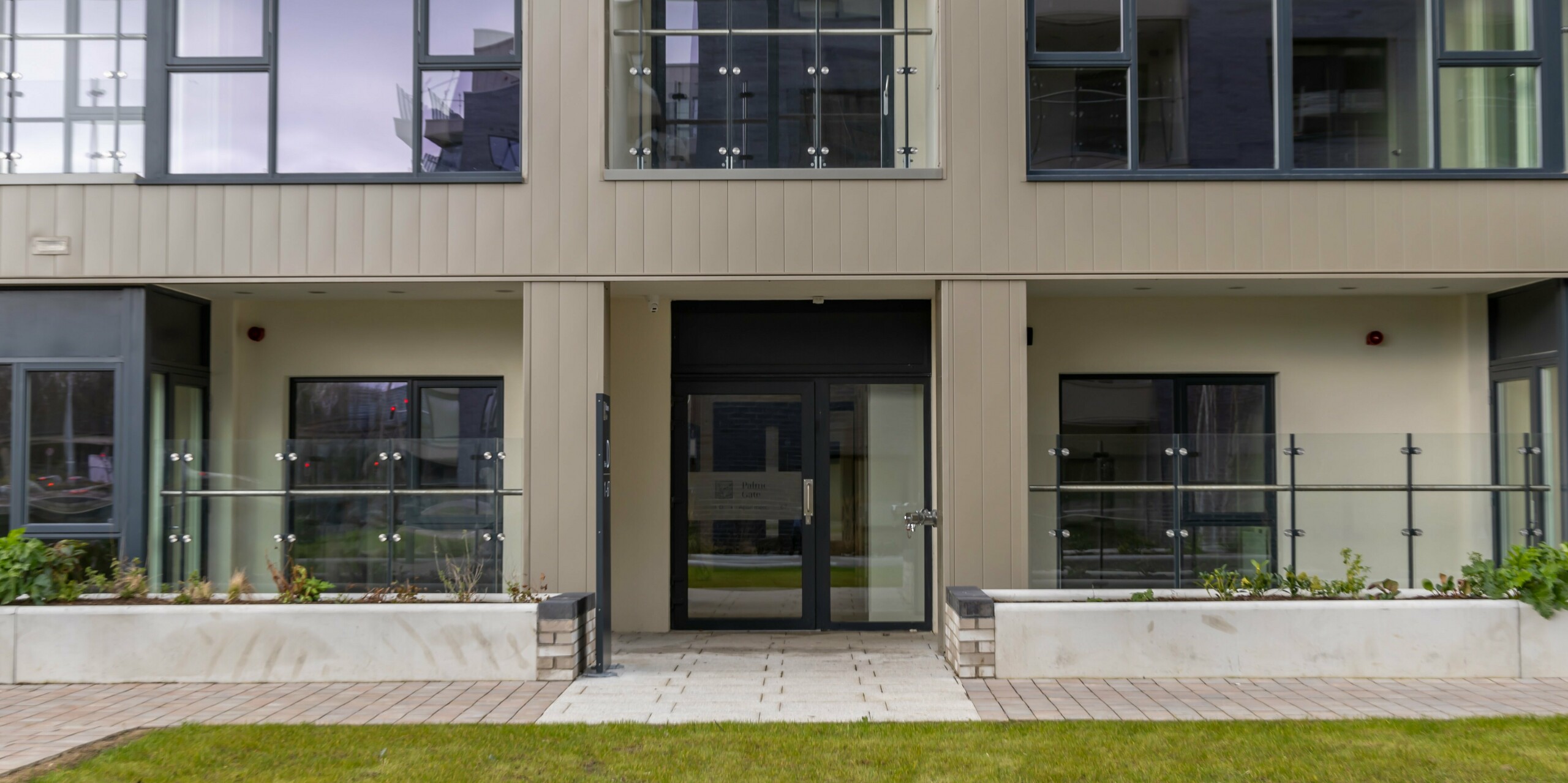 Entrance area of the Palmers Gate residential complex in Palmerstown, Dublin, Ireland. The façade is clad with bronze-coloured PREFA Sidings, giving it a modern and elegant appearance. The entrance area is surrounded by large glass windows and leads to the living areas. Glass balustrades and planters in front of the windows add to the charm of the building. The outer cladding of the apartment blocks consists of a total of approx. 1,700 m² of PREFA sidings and approx. 1,200 m² of the PREFALZ façade system, which is renowned for its robustness and durability.