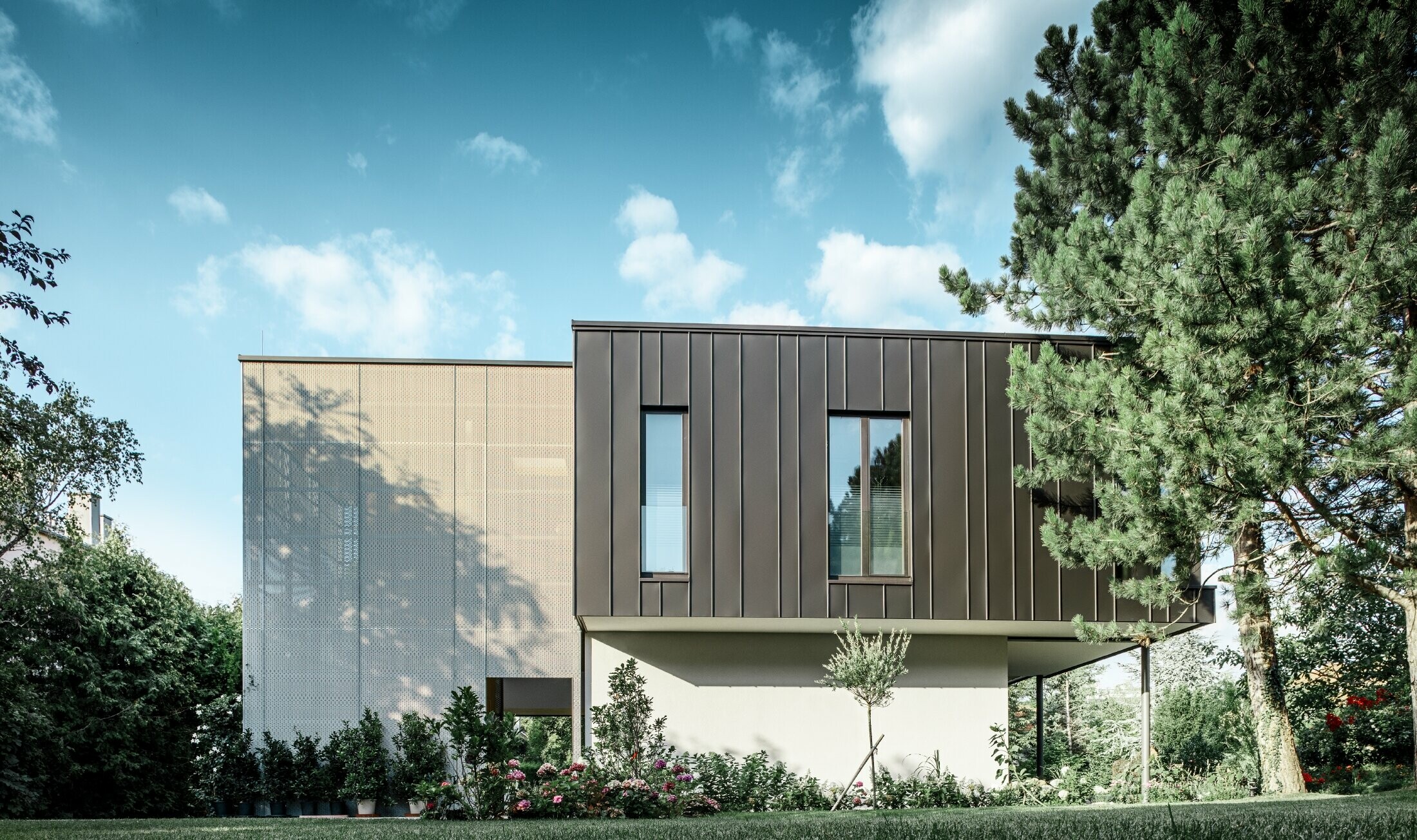 Modern detached house, resembling a tree house, surrounded by an ample garden full of trees, with a modest PREFA single-lock standing seam façade in black grey