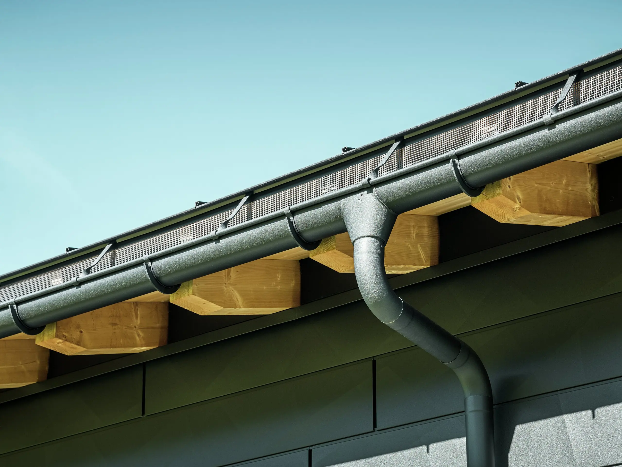 Close-up of the façade of a modern detached house in Ascharina, Switzerland. The sides of the building were clad with striking PREFA Siding.X façade panels in P.10 black. The PREFA roof drainage system with half-round gutter and downpipe is colour-coordinated.
