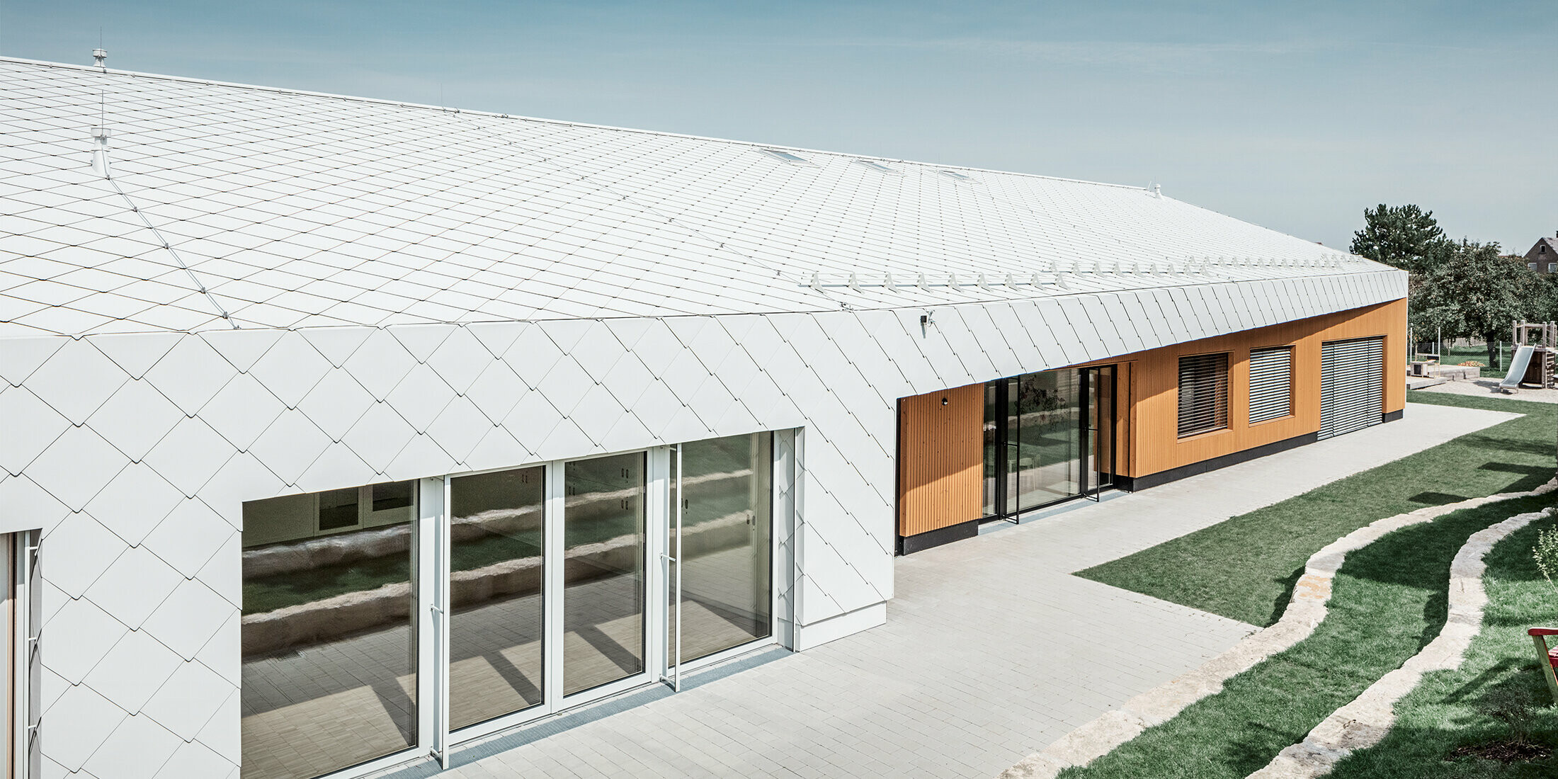 Nursery with the PREFA roof and façade tiles 44 in Prefa white, the roof surface extends over the façade; large window areas