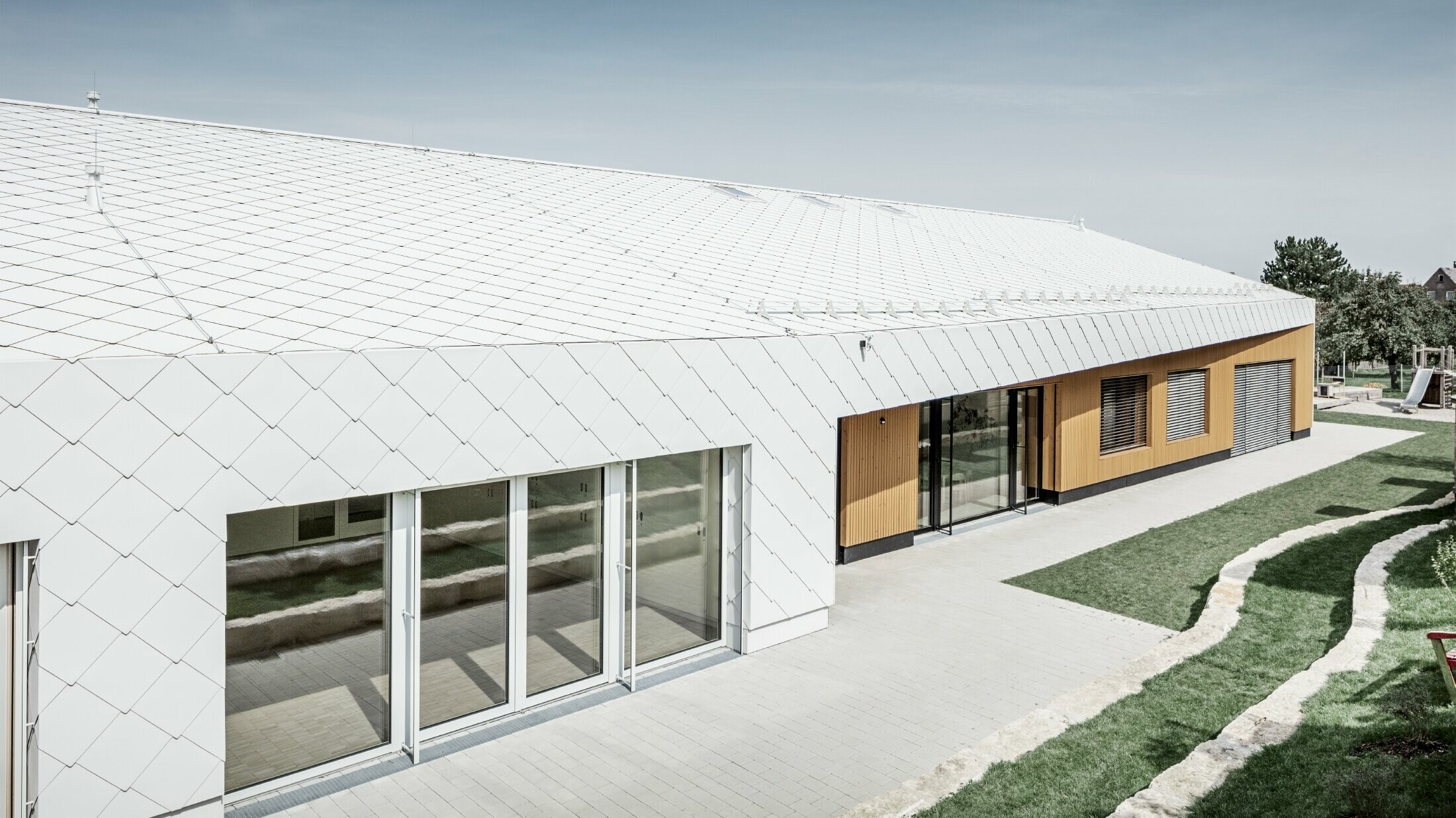 Nursery with the PREFA roof and façade tiles 44 in Prefa white, the roof surface extends over the façade; large window areas