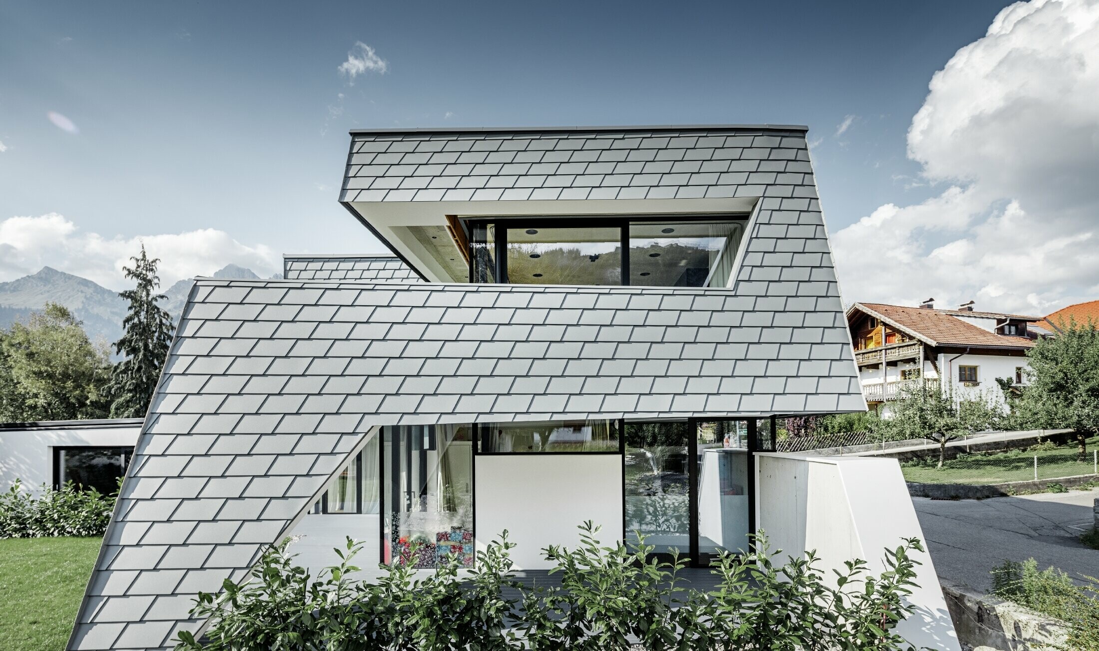 Modern detached house with a flat roof, large windows and a shingle façade in light grey, made of aluminium by PREFA