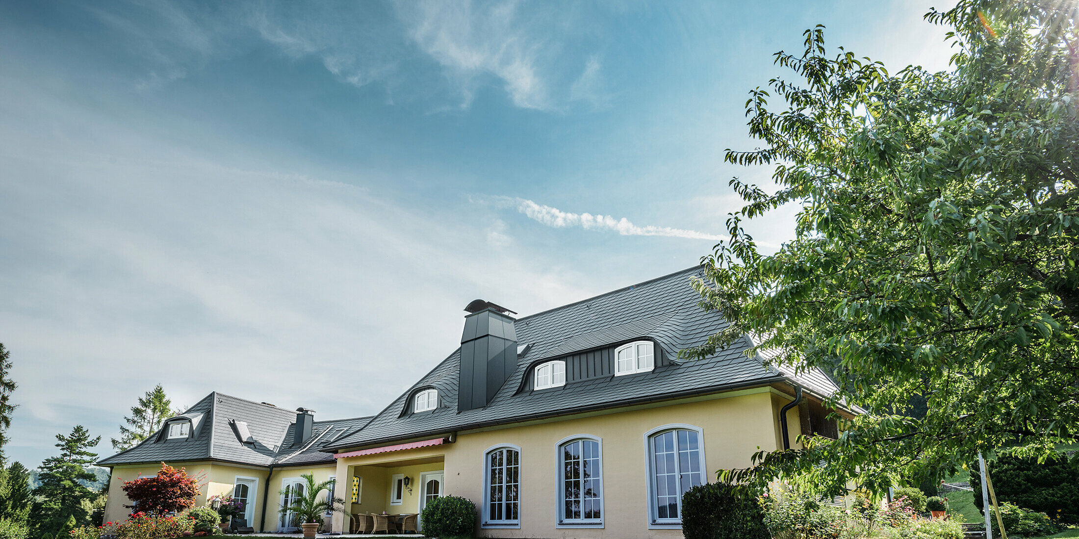 Classic detached house with curved dormers, roofed with the storm-proof PREFA roof shingle, with a 40-year material guarantee.