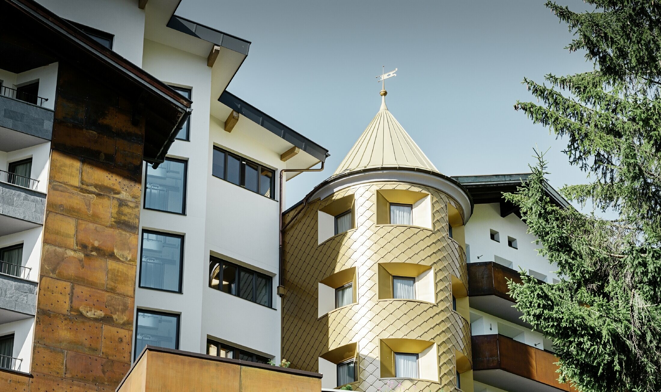 Traditional hotel in Ischgl (Austria) with wooden balconies, a wooden façade and tower clad in PREFA gold-coloured aluminium panels