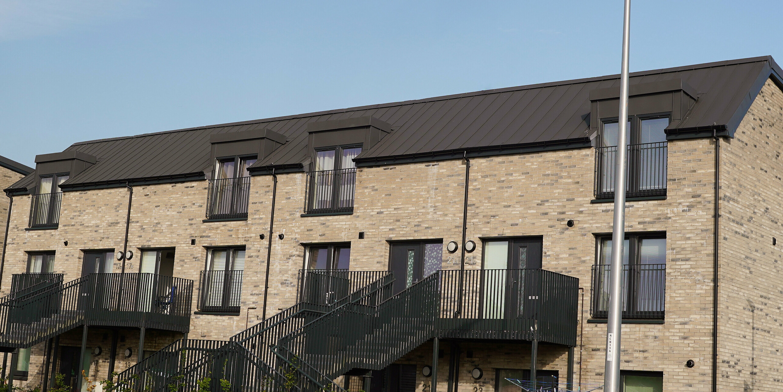 Detailed view of a modern residential complex in Edinburgh, Scotland, with a high-quality PREFALZ roof system in P.10 dark grey. PREFA's durable aluminium roofs offer an optimum combination of functionality and aesthetic design that integrates seamlessly into the urban architecture. The visible material quality and precise workmanship of PREFALZ products contribute to increasing the value of the property and emphasise the sustainability of modern construction projects. As a counterpart to the contemporary roof, the building is adorned with a traditional brick façade.