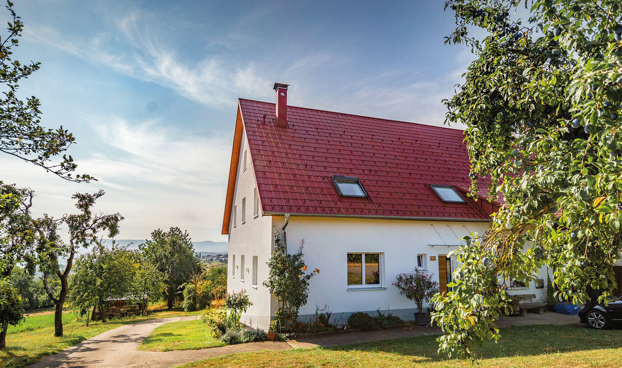 Romantic rural cottage surrounded by trees and shrubs. Covered with a PREFA roof in oxide red.