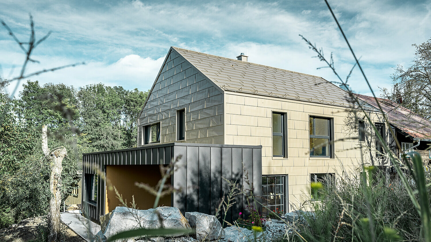 Apartment complex without eaves is clad on the roof and façade with the PREFA FX.12 aluminium panel in bronze. Right next to it is a garage with a flat roof with an angled standing seam façade.