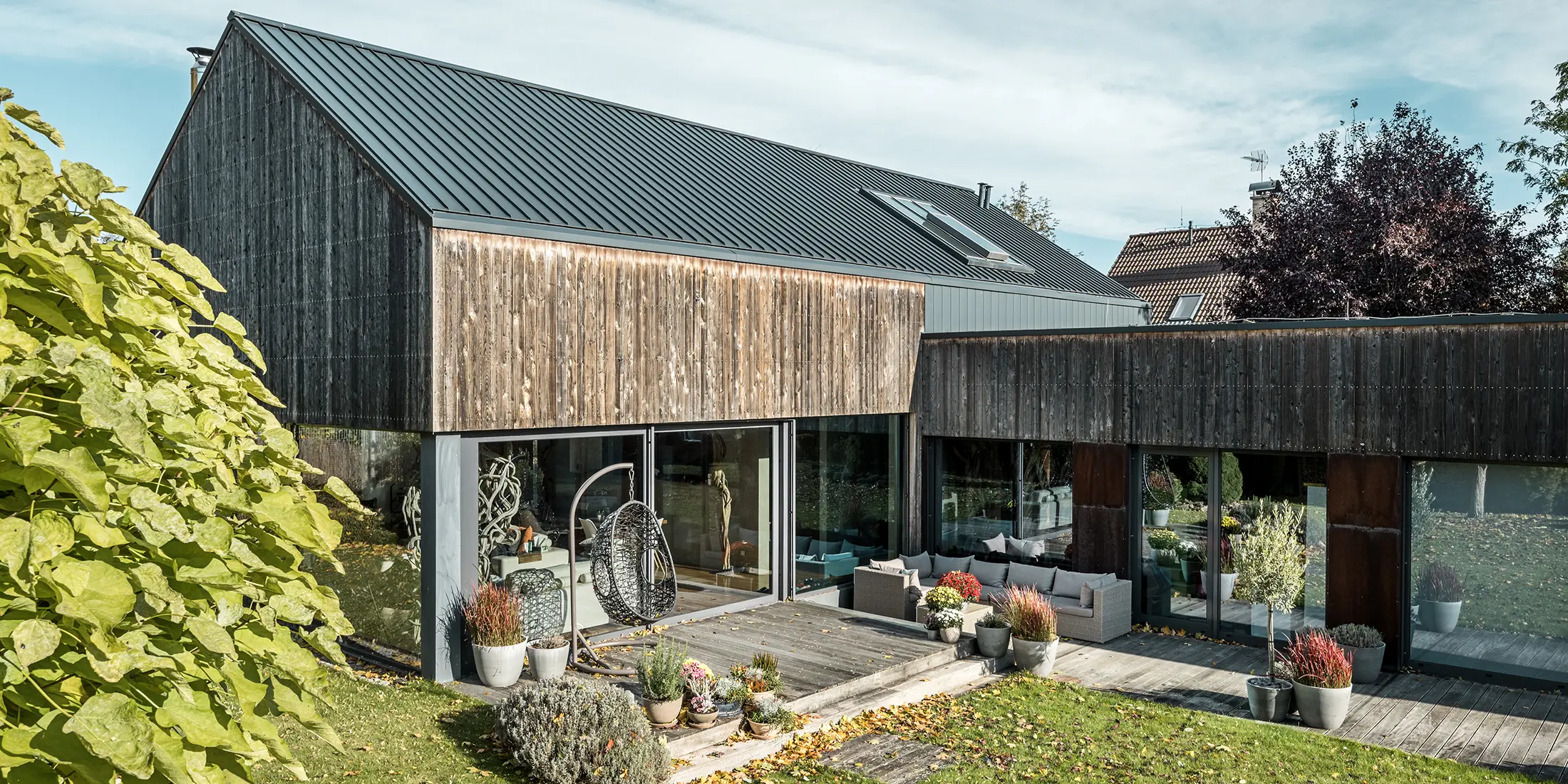 Detached house with gable roof, covered with PREFALZ double standing seam in anthracite and weathered wooden façade. With a beautiful wooden terrace and large windows on the ground floor.