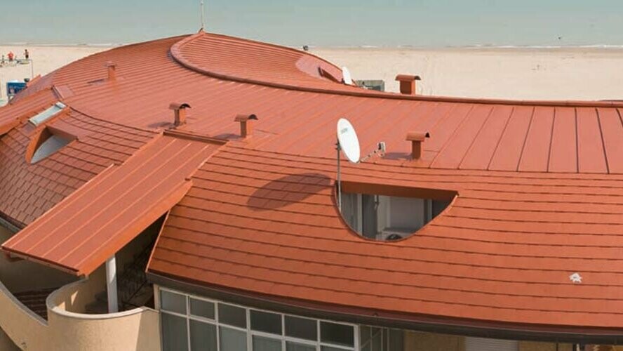 Rounded roof in residential complex, covered with PREFA roof shingles and standing seam roof - PREFALZ from PREFA in brick red.