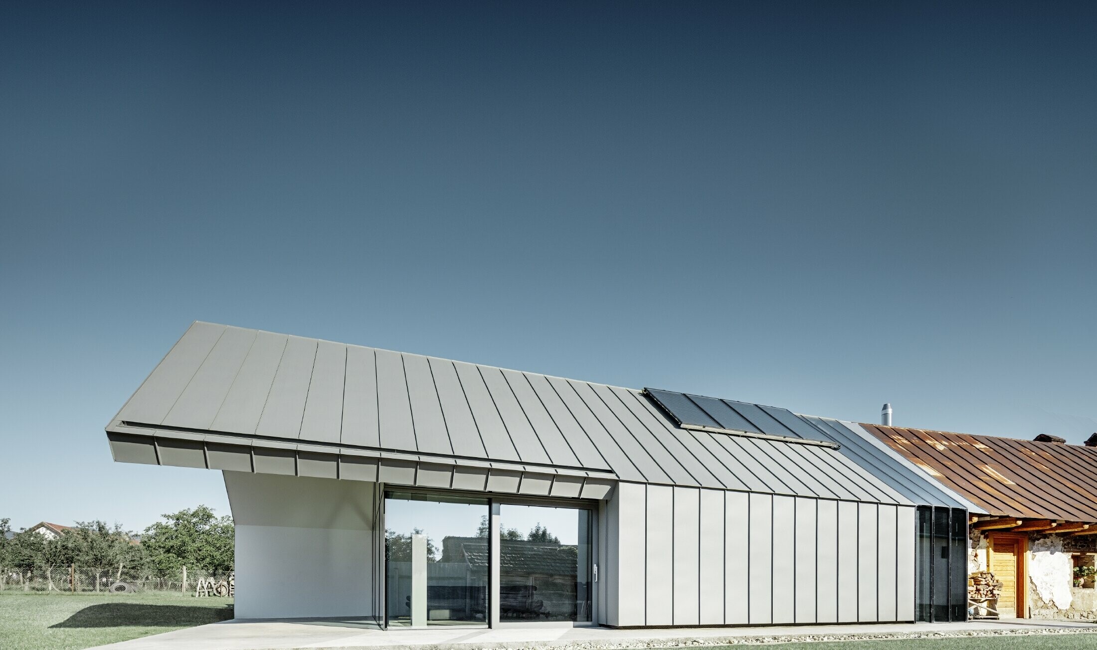 Modern architect’s office and detached house adjoining an old farmhouse with a stone façade, clad in PREFA standing seam and single lock standing seam in light grey