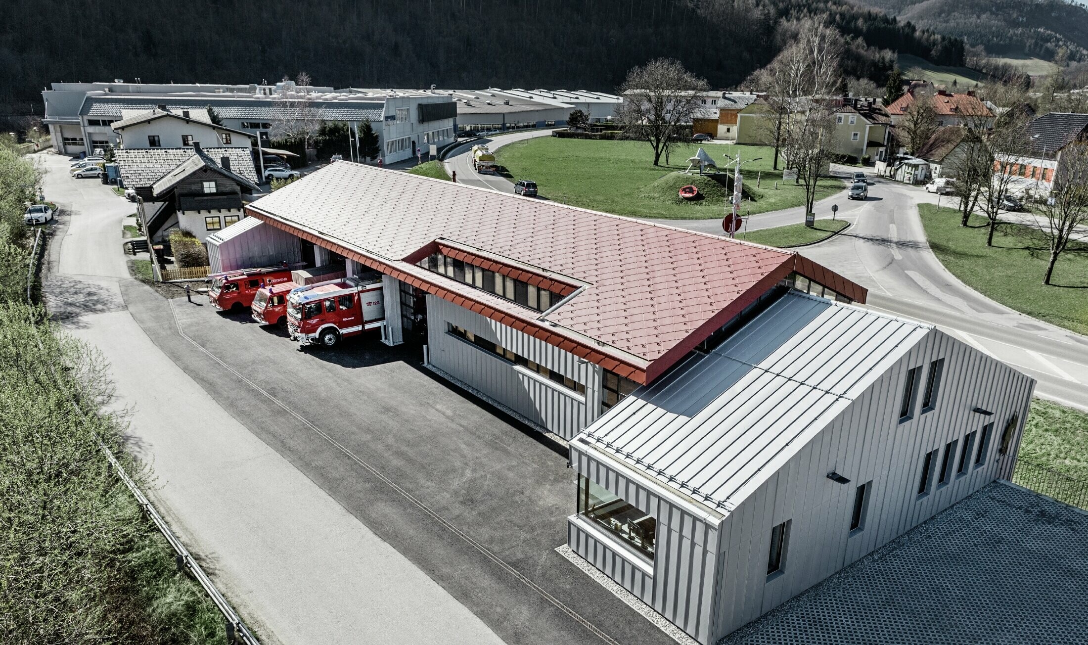 Aerial view of the company fire station in Marktl/Lilienfeld. The roof and façade of the left part of the building was completely clad in rhomboid tile 44 in oxide red. The right part is covered in an aluminium cladding with Prefalz in metallic silver.