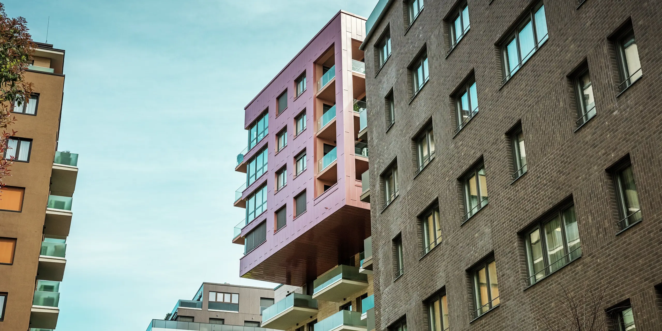 Blick auf das prägnante, auskragende Gebäudeelement des Grand Corvin Projekts im Budapester Corvin-Viertel. Die oberen Etagen sind mit PREFA Siding Fassadenpaneelen in vertikaler Verlegung und der Sonderfarbe Lachsmetallic verkleidet. Die langlebige Aluminiumfassade hebt sich deutlich von der umgebenden Ziegelarchitektur ab und unterstreicht den modernen, architektonischen Charakter des revitalisierten Stadtteils.