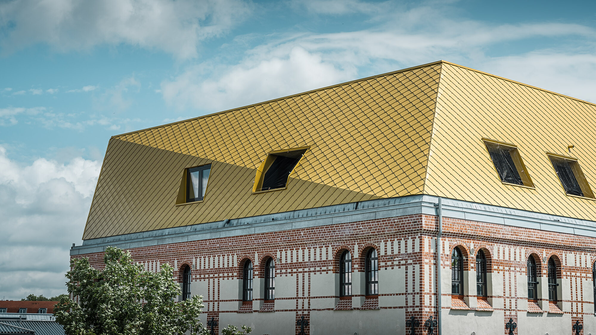 The roof with the Maya gold aluminium rhomboid tiles and a fold from up close, part of the listed façade can be seen.