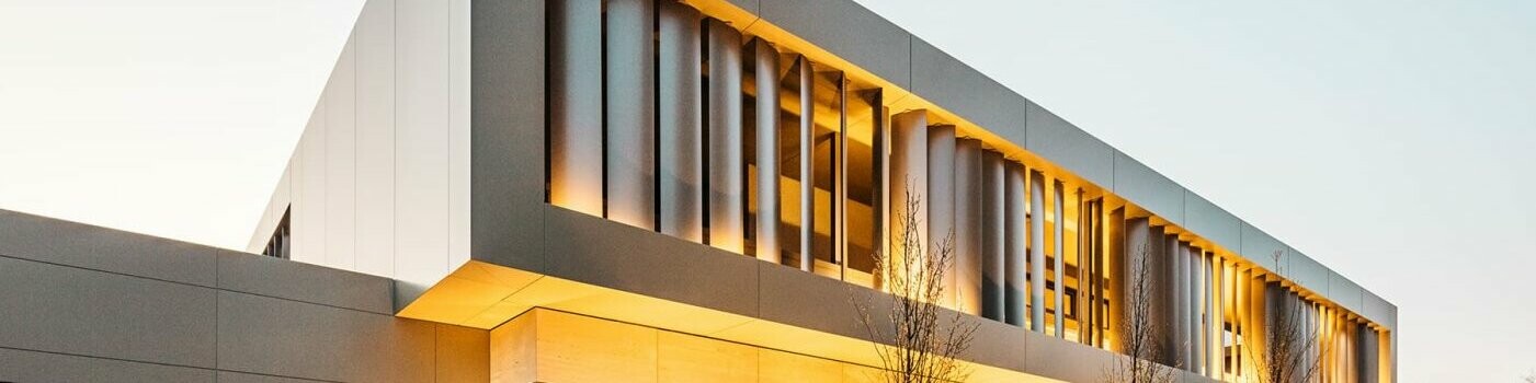 Street view at night, garage with bronze-coloured façade on the left, stone façade below, bronze-coloured aluminium façade with slats inside above