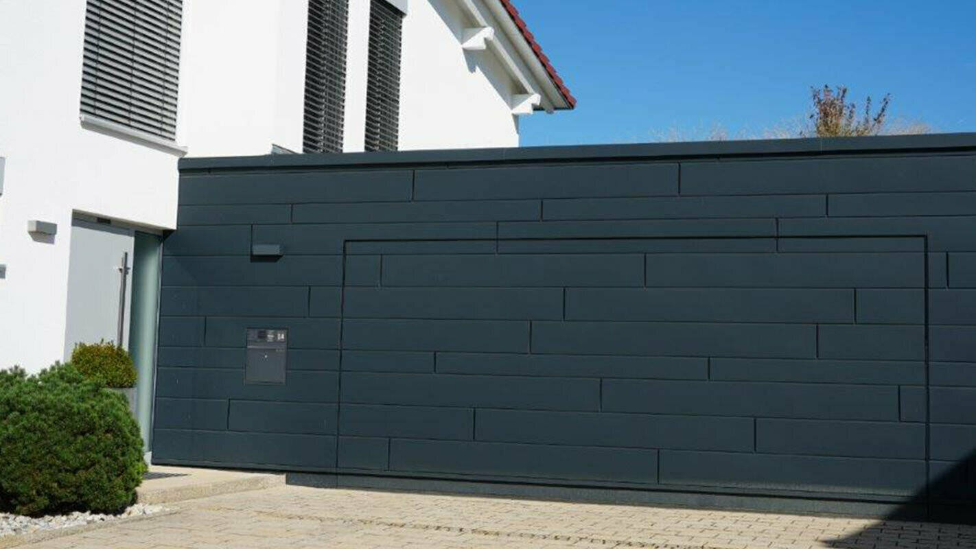 Façade of a garage after renovation with PREFA sidings in anthracite; garage door is installed flush to the façade 