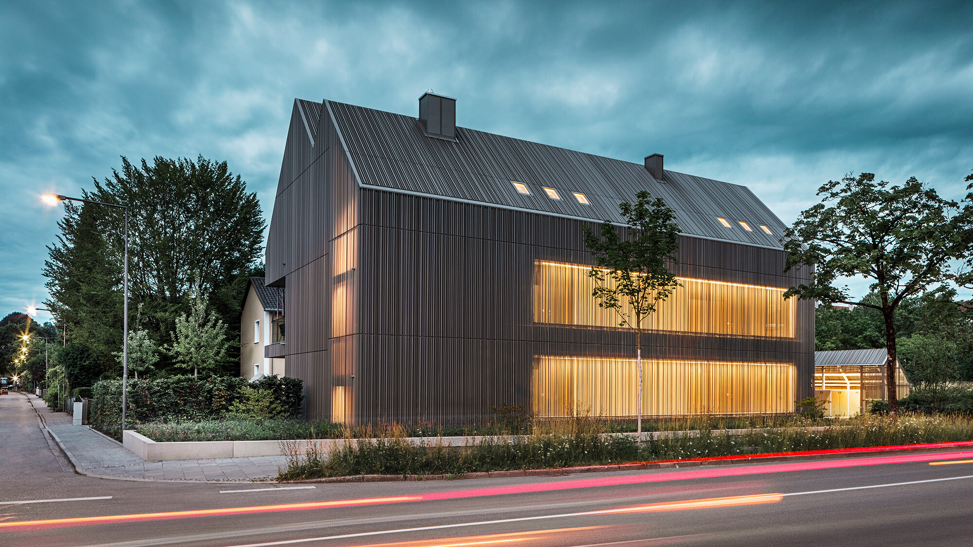 Shot of the house in the evening from the street side, the permeable quality of the roof and façade can be seen.