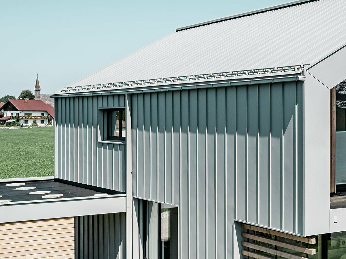 Detached house with gable roof, with PREFALZ on the roof and façade; for roof drainage, the PREFA box gutter is used with the PREFA square downpipe in the special colour patina grey.