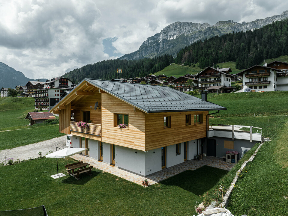 Das Einfamilienhaus Casa Hoffe in der alpinen Gemeinde Sappada, Italien, zeigt ein harmonisches Zusammenspiel von traditioneller und moderner Architektur. Ausgestattet mit PREFA Dachplatten R.16 in P.10 Schwarz, die Stabilität und Eleganz verleihen, während die Siding.X Fassadenpaneele im Eingangsbereich das Design mit einer extravaganten Note bereichern. Die langlebigen Aluminiumelemente von PREFA integrieren sich nahtlos in die für die Region typische Holzfassade und bieten dauerhaften Schutz inmitten der idyllischen Berglandschaft.