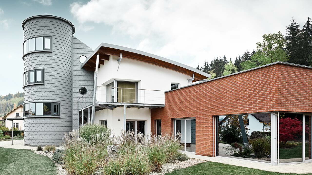 Detached house with tower extension, the round tower is clad with PREFA façade shingles in patina grey 