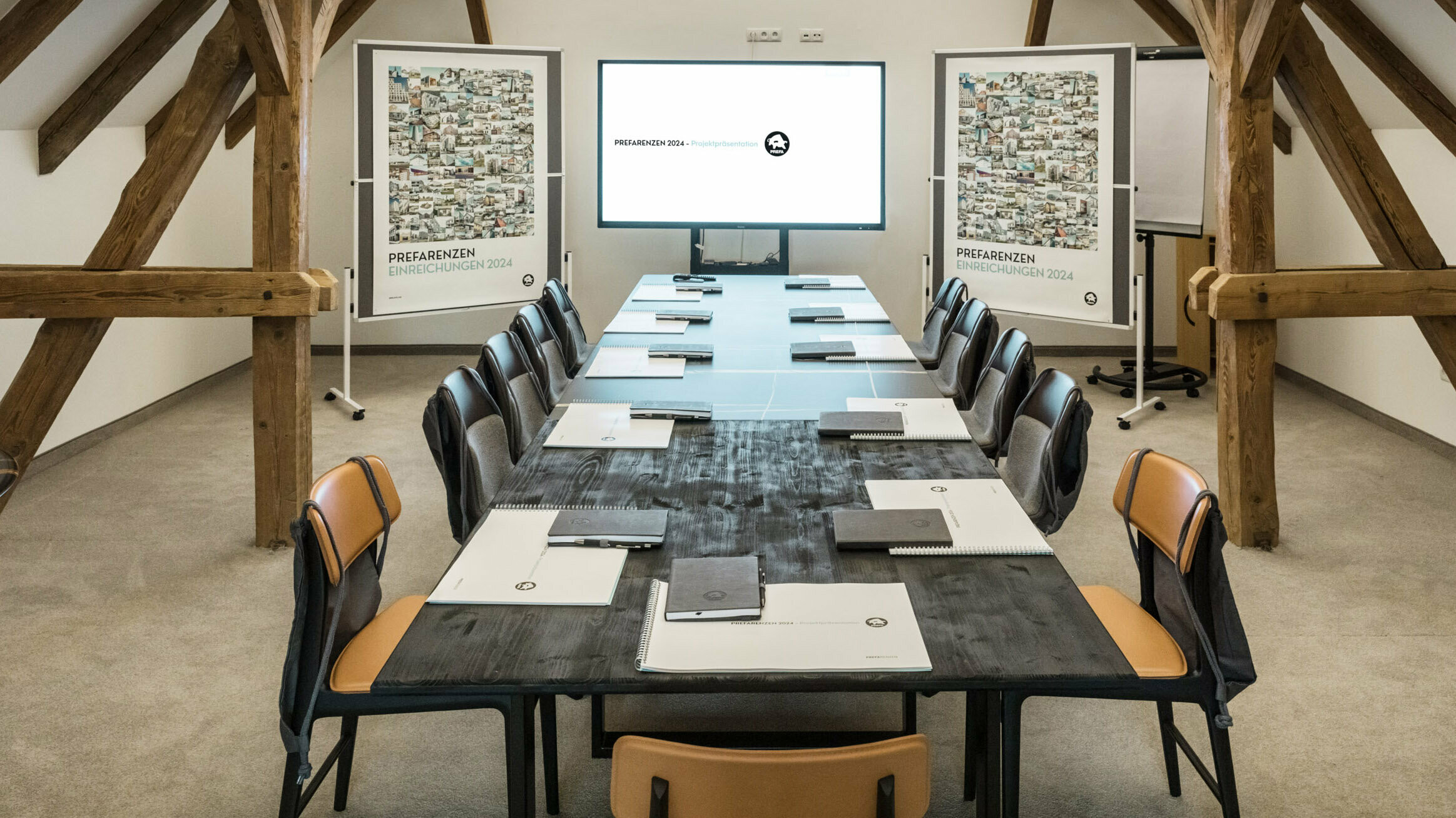 Frontal view of the meeting room: The screen, posters, project folders and notebooks are in view.