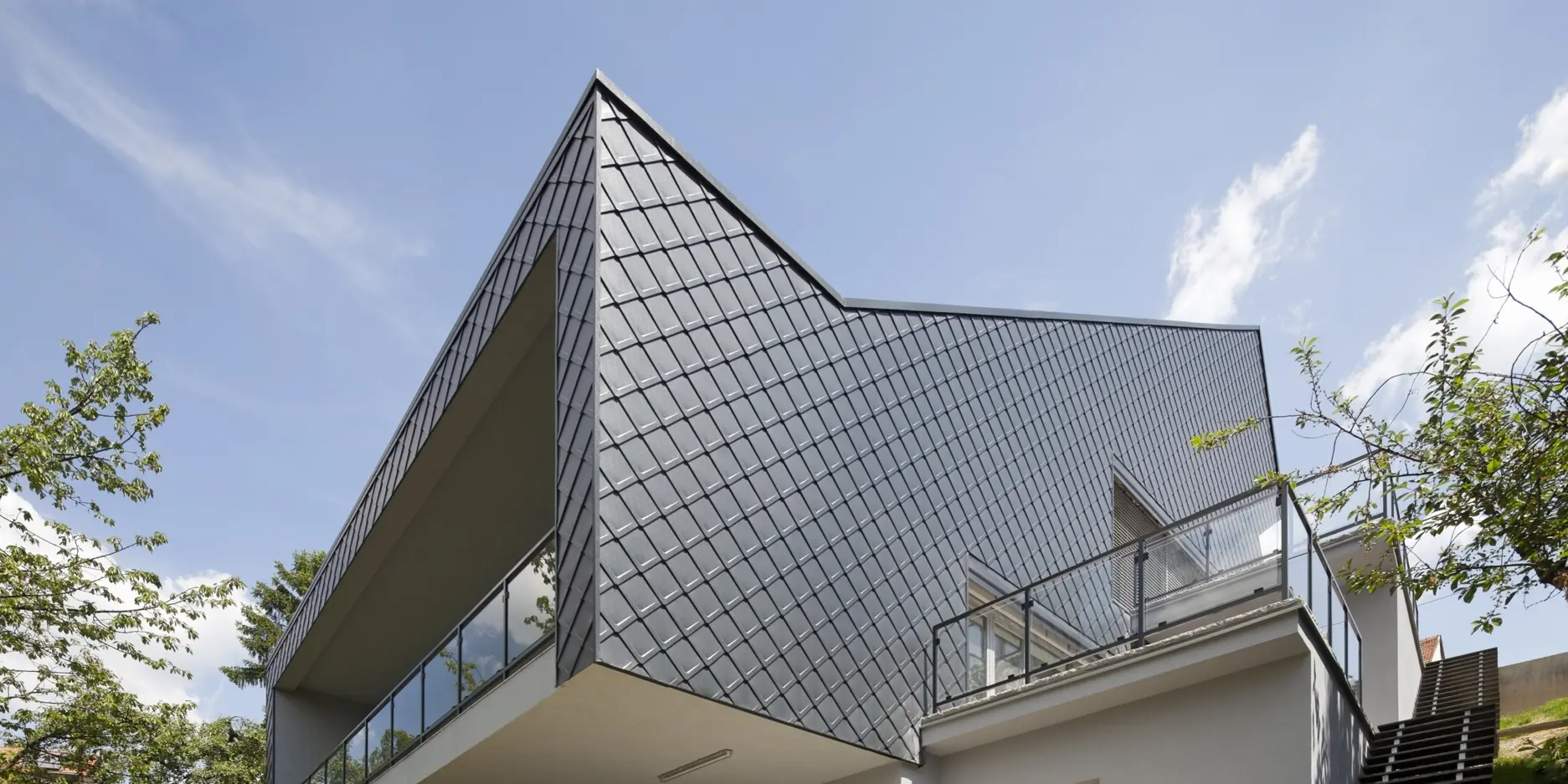 Ein modernes Wohnhaus in Zagreb, aufgenommen aus der Froschperspektive. Das stilvolle Einfamilienhaus wurde mit robusten PREFA-Blechrauten in Anthrazit verkleidet. Die hochwertige Aluminiumhülle sorgt für Langlebigkeit und ein elegantes Erscheinungsbild. Die überdachte Terrasse ist das Highlight der Gebäuderückseite.