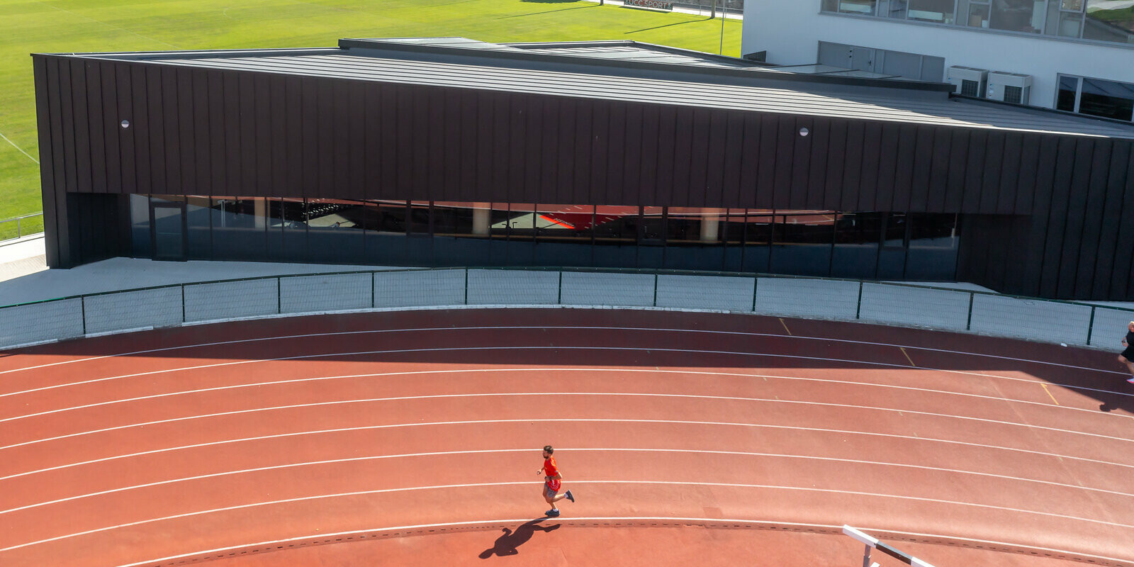 In the background of the running track is a triangular building with a PREFA aluminium shell in black