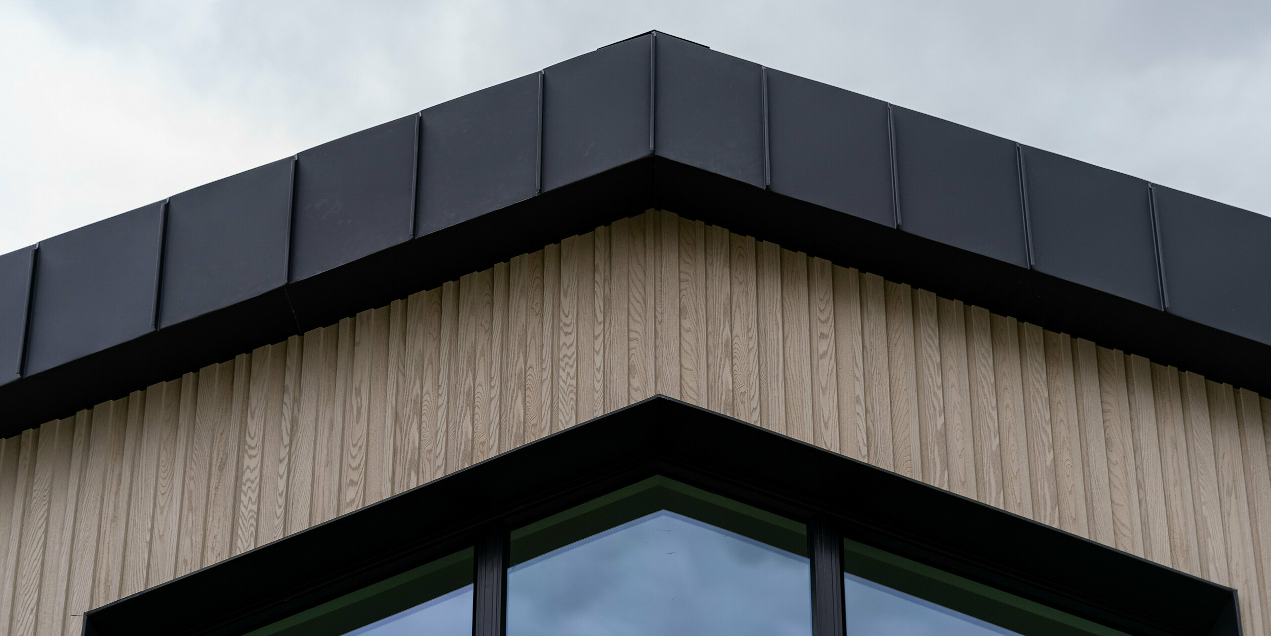 Close-up of the gable end of the modern detached house ‘The Hide’ in Cornwall with a generous glass façade and high-quality PREFALZ standing seam roofing made of aluminium in P.10 anthracite. The clear architecture harmoniously combines the internal and external spaces, while the PREFALZ material provides elegant weather protection.