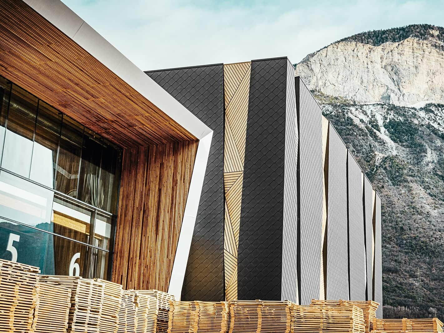 Rothoblaas industrial building with PREFA Rhomboid façade tile 44 × 44 in P.10 Black surrounded by a gigantic mountain backdrop.