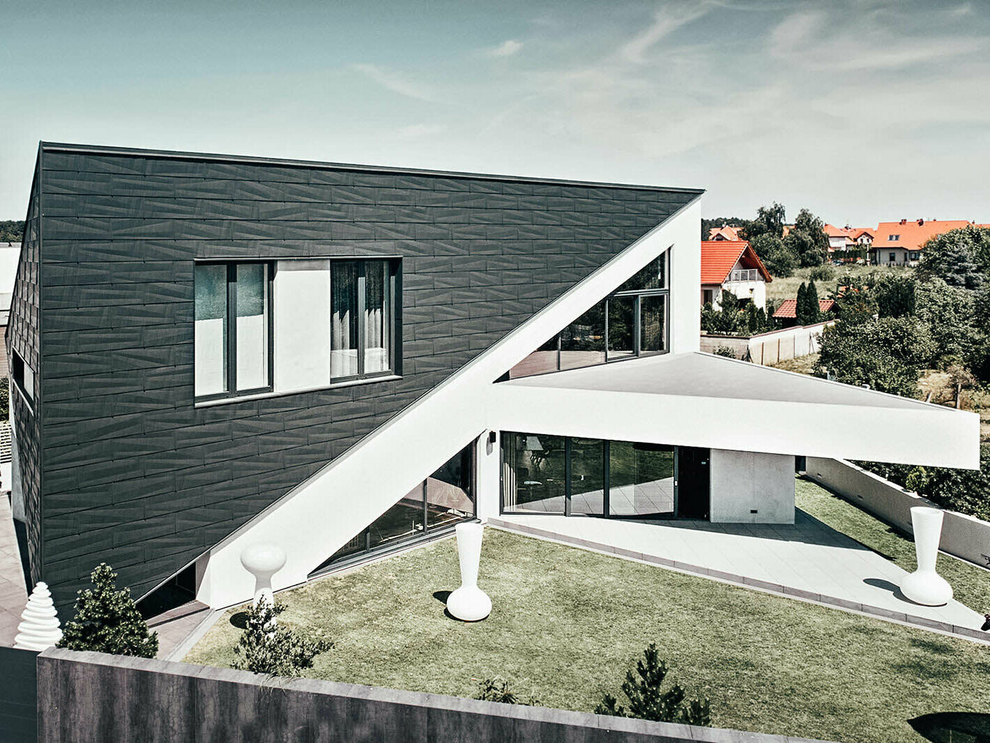 Lateral view of the triangle house in Poland. It is covered in PREFA Siding.X façade panels, which matches the white contrast of the rest of the house.
