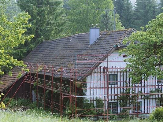 Old roof on a rural cottage (with scaffolding) just before the roof was renovated with PREFA shingles