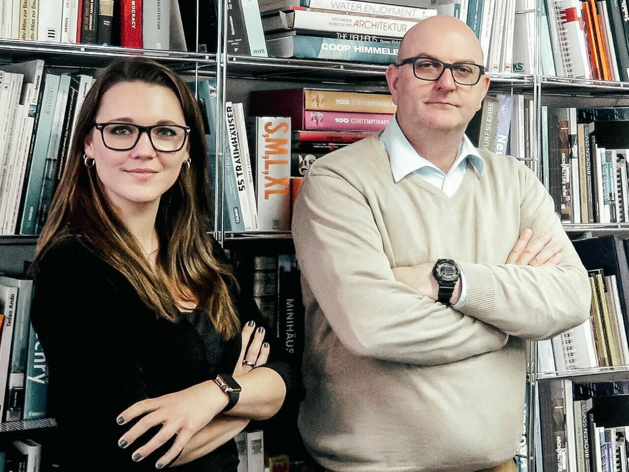 A portrait of architect Jens-Uwe Lau and project manager Kristin Prelec, standing in front of a bookcase
