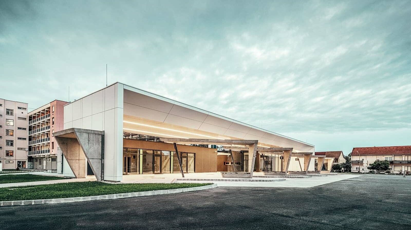 The photo shows the entire railway station at dusk. The waiting areas can be viewed from the side view. The PREFABOND composite panels on the façade in the colour pure white complement the overall picture.