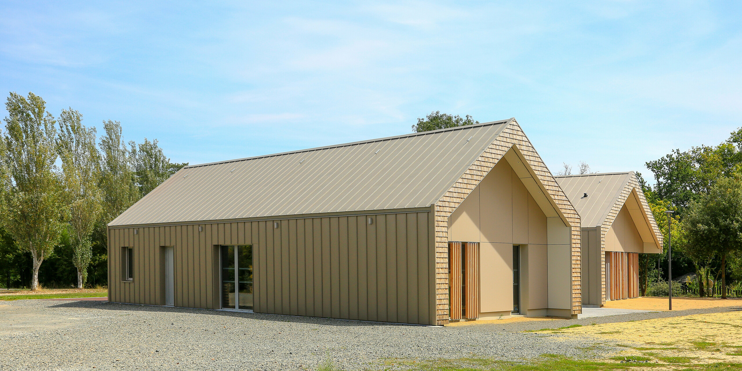 Modernes Jugendzentrum in Mûrs-Erigné, Frankreich, mit langlebiger PREFALZ Dach- und Fassadenverkleidung in Bronze. Die Stehfalzdeckung aus Aluminium von PREFA besticht durch hohe Witterungsbeständigkeit und elegante Optik - ideal für nachhaltige und wartungsarme Bauprojekte. Die edle Farbgebung zeigt eine perfekte Integration in die Umgebung.