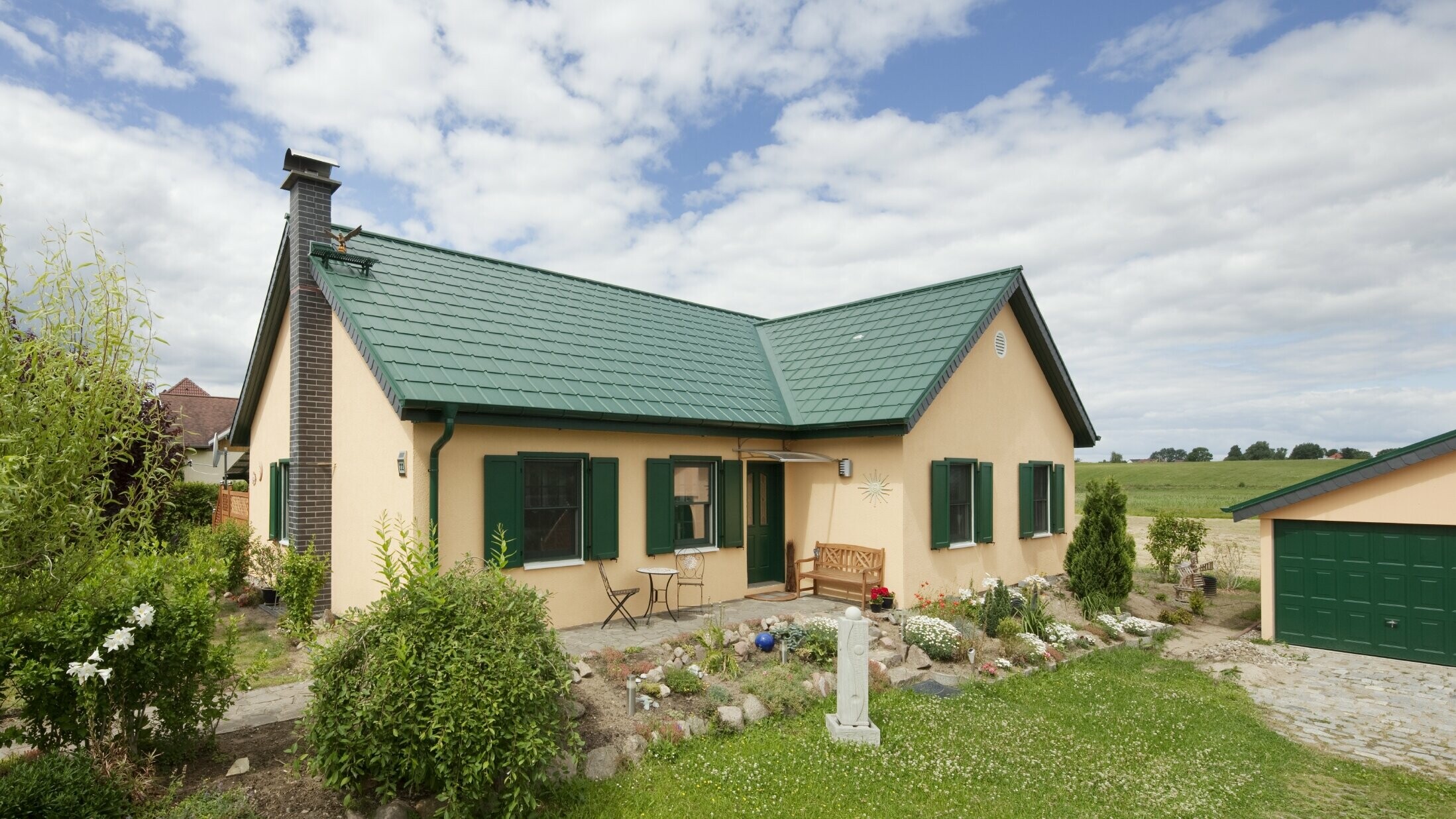 Extended gable roof; L-shaped gable roof; with PREFA roof tiles in P.10 moss green; pretty rural cottage with green shutters to match the PREFA roof.