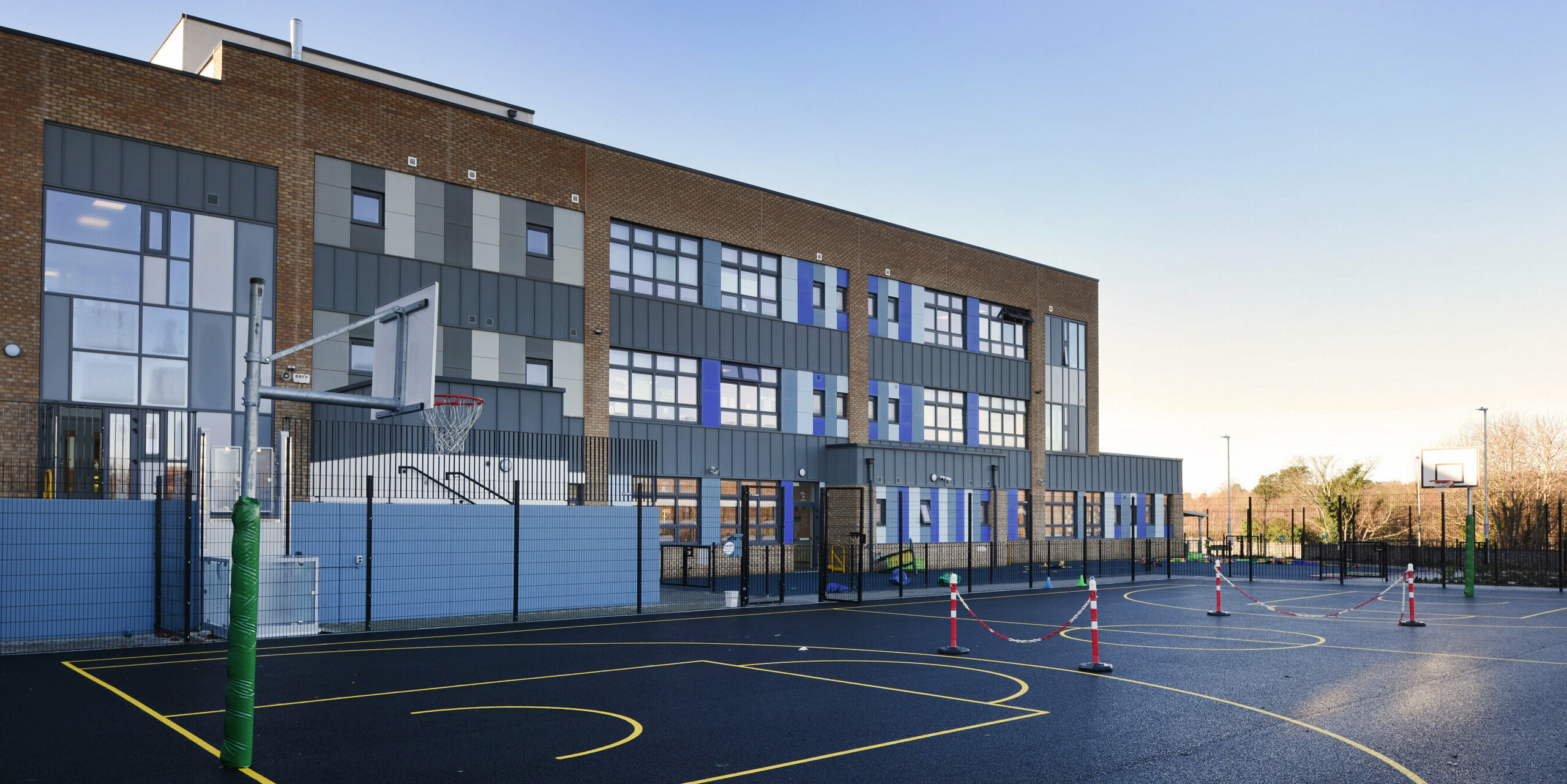 Rear of the Pelletstown Educate Together National School in Dublin, overlooking the basketball court. The light grey aluminium cladding made from PREFALZ P.10 light grey complements the school's brick façade and offers weather-resistant protection and a modern design.