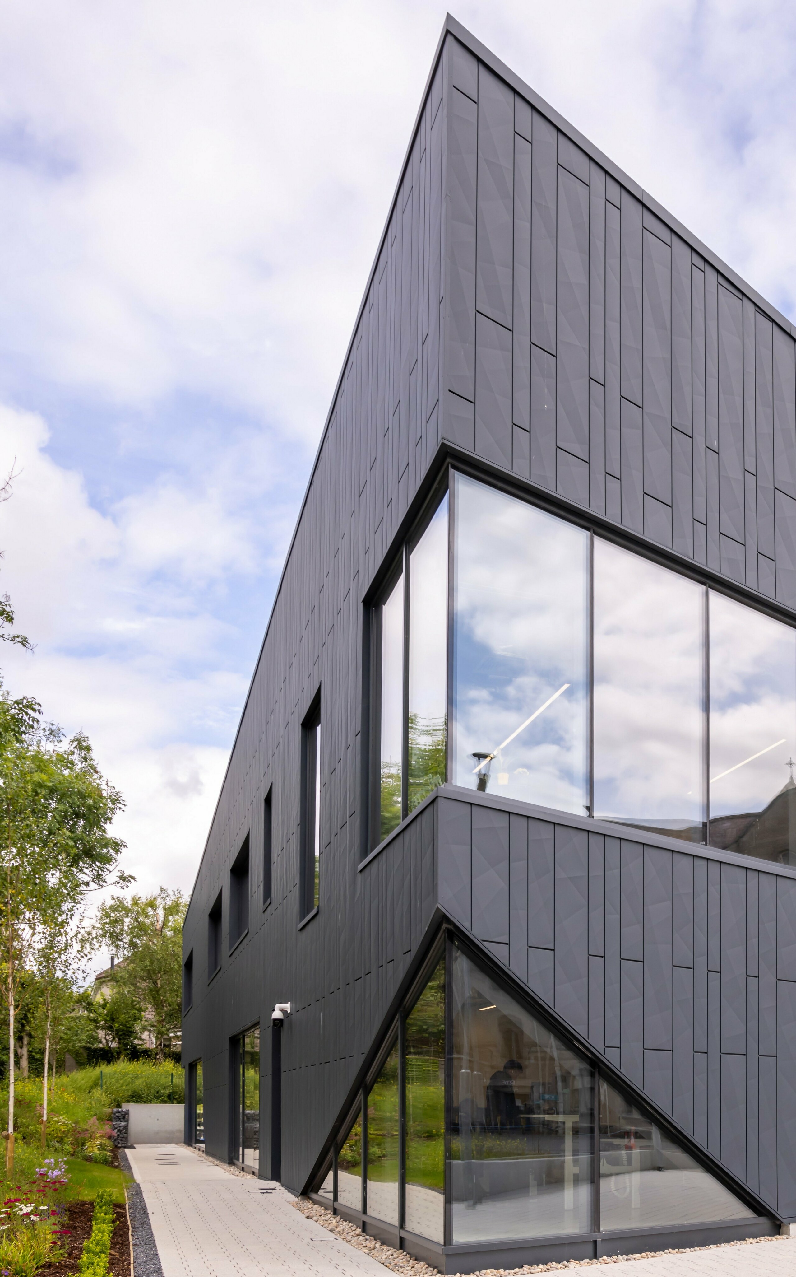 View of the front of the CREW building in Galway, Ireland, with a modern façade made of PREFA Siding.X façade panels and PREFALZ in the colour P.10 anthracite. The vertical lines of the façade and the large window areas emphasise the innovative and dynamic design of the building. The aluminium cladding blends harmoniously into the surrounding landscape and underlines the high-quality architecture of the building.