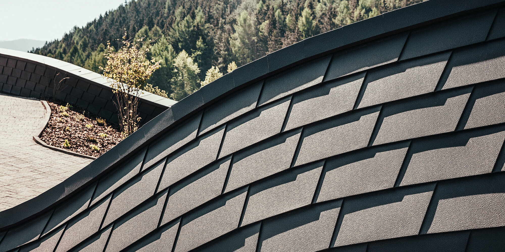 Detailed view of PREFA façade shingles in P.10 Brown. A section of the forest can be seen in the background