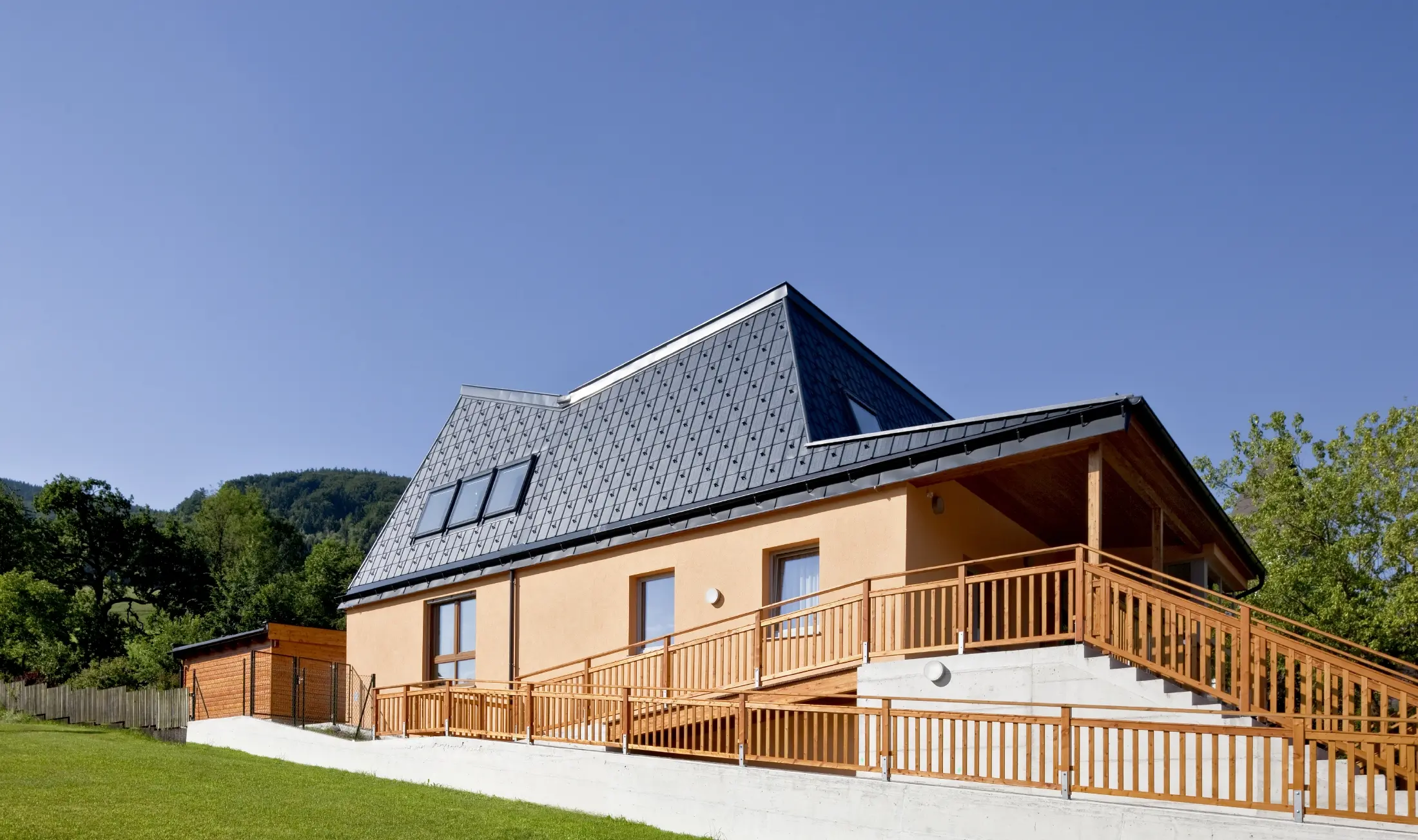 Kindergarten with orange rendered façade and a roof full of nooks and crannies, covered with PREFA roof tiles in P.10 anthracite;
