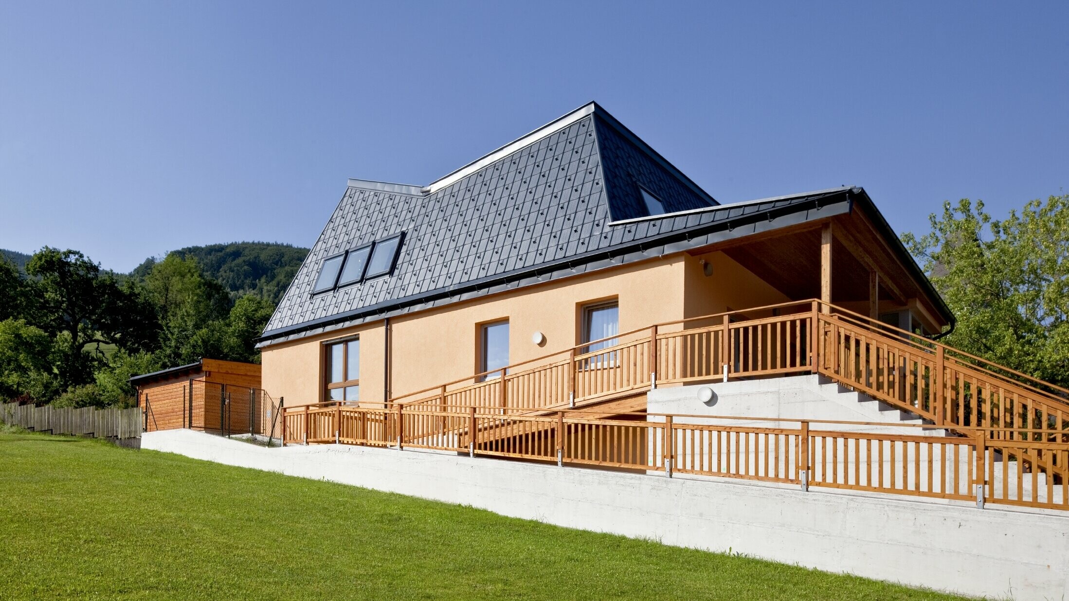 Kindergarten with orange rendered façade and a roof full of nooks and crannies, covered with PREFA roof tiles in P.10 anthracite;