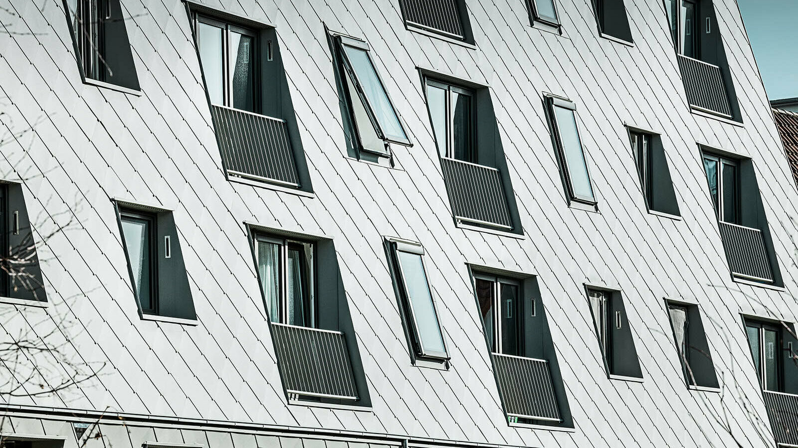 The picture shows the zinc-grey PREFA rhomboid façade tiles in P.10, which decorate the façade of the building.