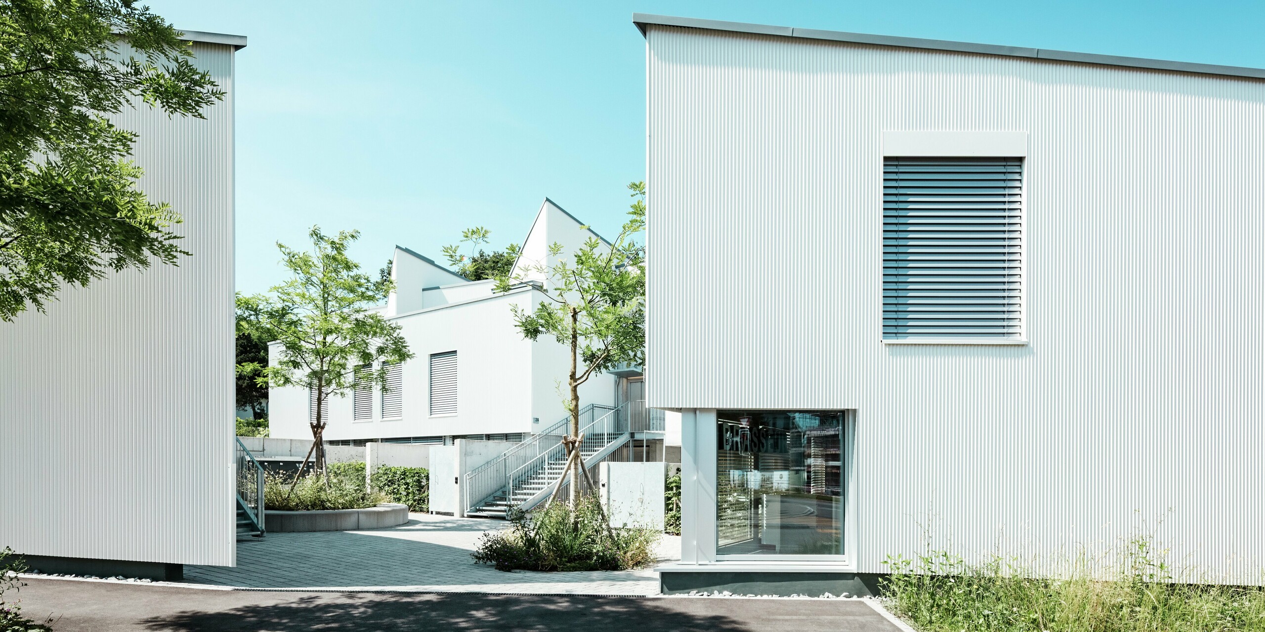 Ein Ensemble moderner Tiny Homes mit klarer Formsprache, verkleidet mit dem filigranen PREFA Zackenprofil in P.10 Reinweiß. Die vertikale Struktur der Aluminiumfassade sorgt für Tiefe und Leichtigkeit, während die Raffstores für Funktionalität und Design stehen. Die witterungsbeständige PREFA Hülle bietet Langlebigkeit und zeitlose Eleganz.