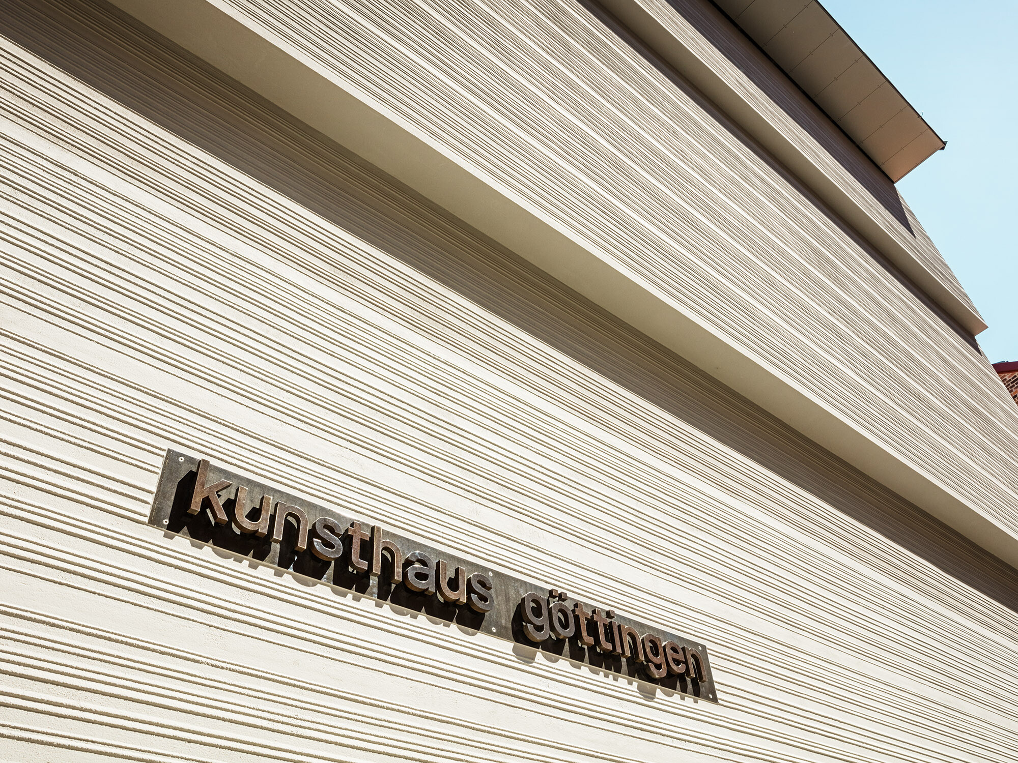 A close-up of the comb plaster façade with "kunsthaus göttingen" written on it in small, bronze letters. 