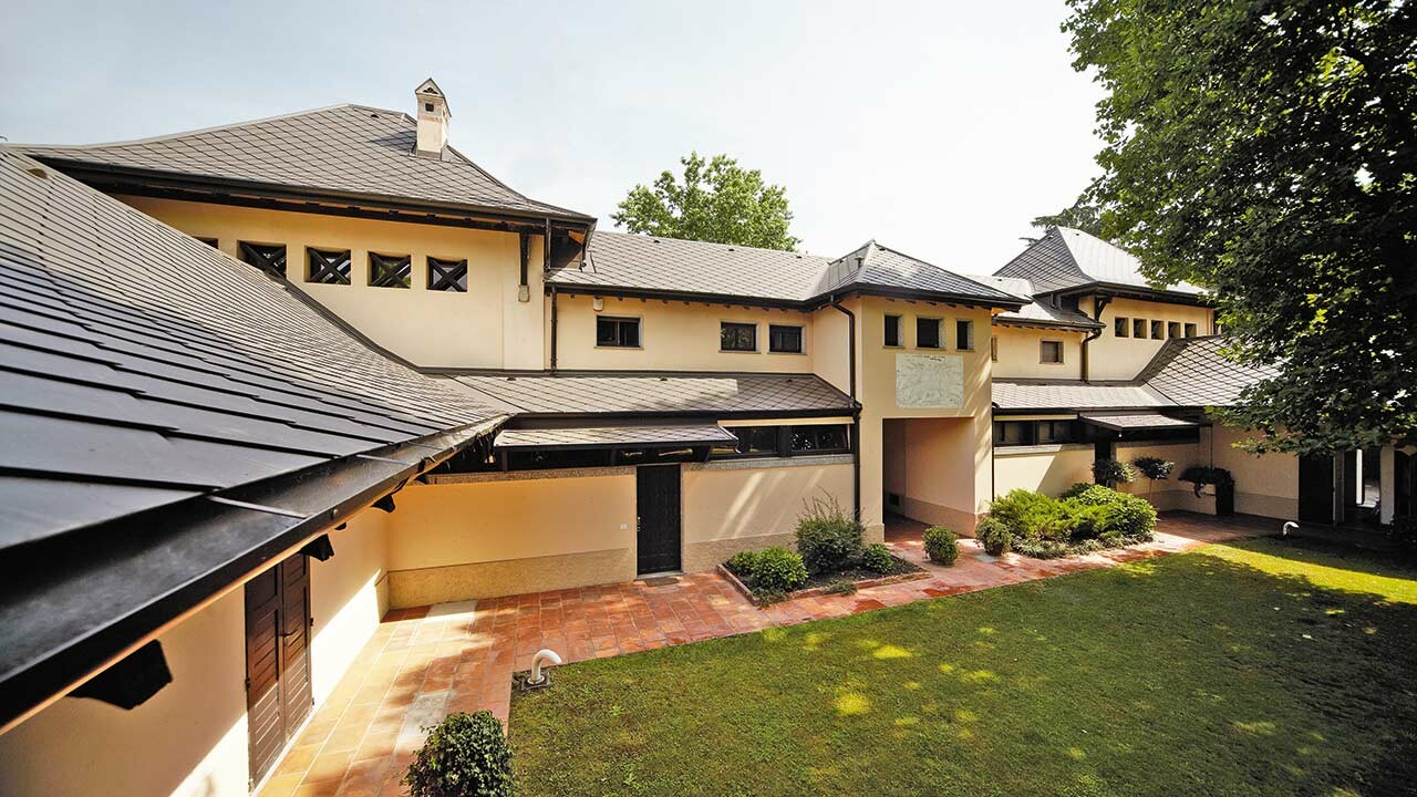 Italian villa with rhomboid roof in P.10 brown by PREFA with beige façade colour with shady inner courtyard