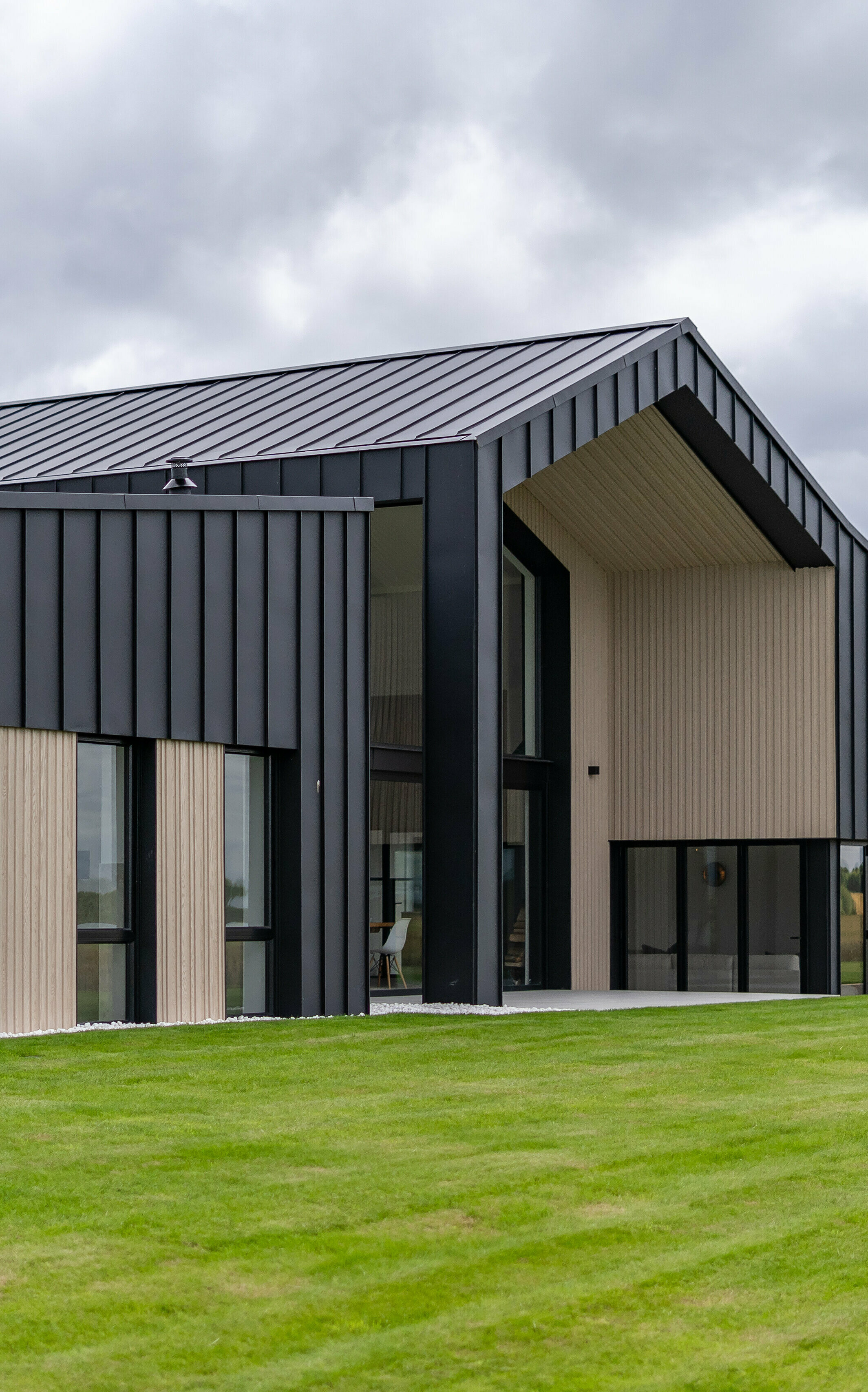 An oblique view of the rear of the detached house ‘The Hide’ in Cornwall, emphasised by the PREFALZ aluminium facade in P.10 anthracite. The precise standing seam covering made of high-quality metal sheets forms an elegant contrast to the wooden elements, while the generous roof with its clear lines underlines the modern architecture of the building. Surrounded by well-kept greenery, the design blends harmoniously into the landscape.